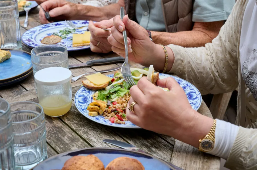 Handen met een vork boven een bord salade aan een gedekte houten tafel