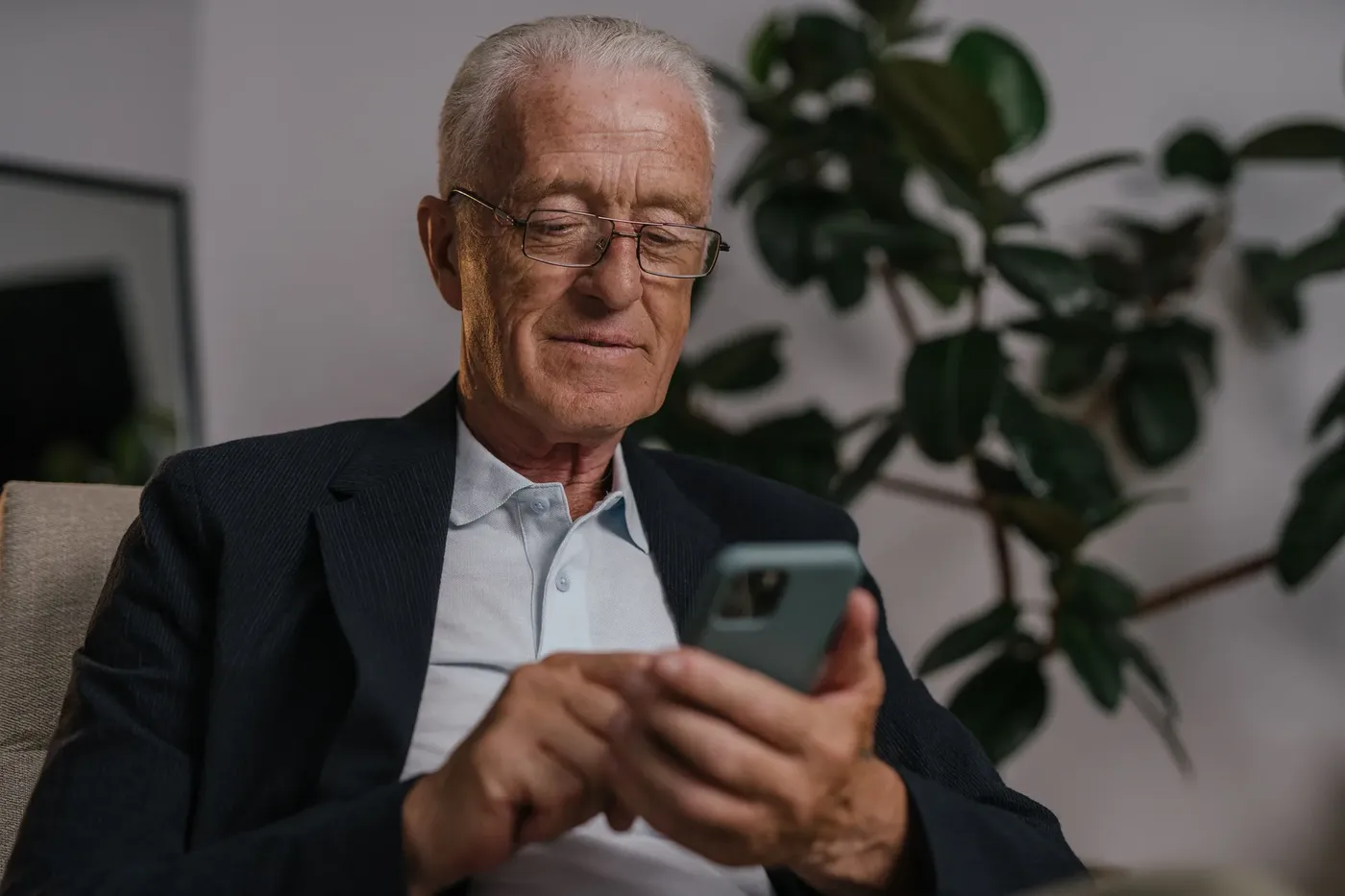 Oudere man met bril kijkt glimlachend op zijn telefoon
