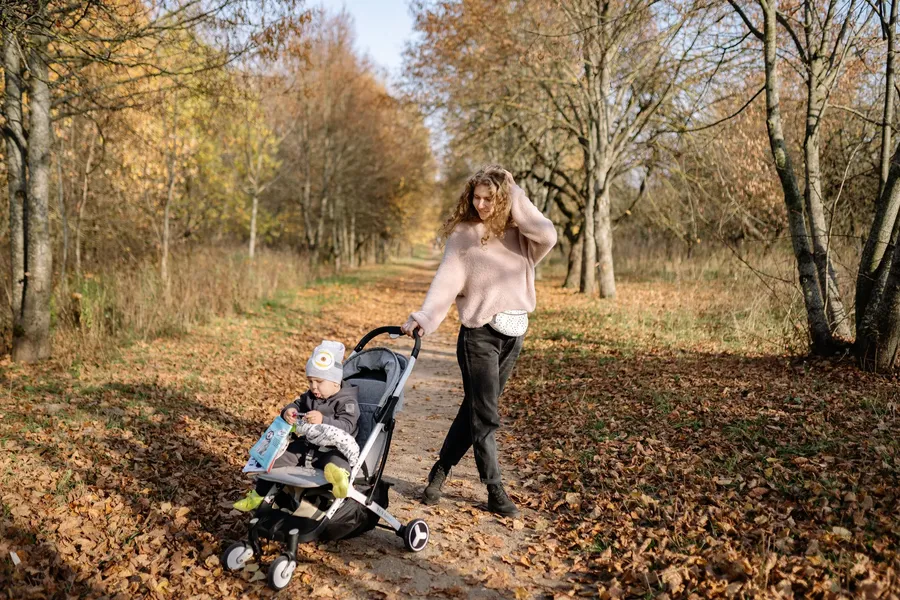 Moeder wandelt met kinderwagen over een herfstig parkpad