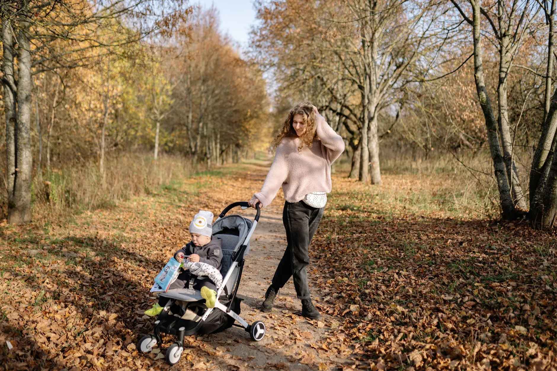 Moeder wandelt met kinderwagen over een herfstig parkpad