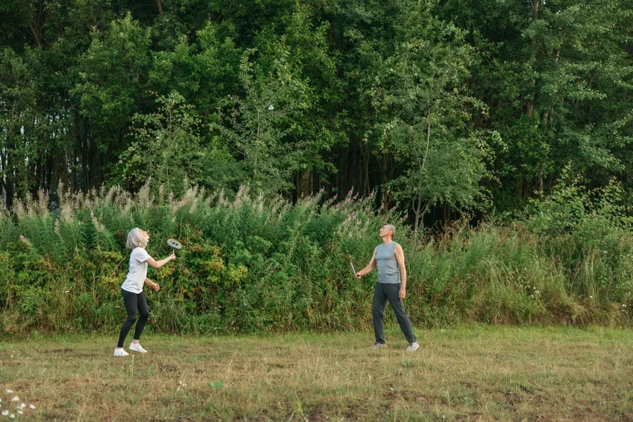 Een ouder stel speelt samen badminton in de buitenlucht.