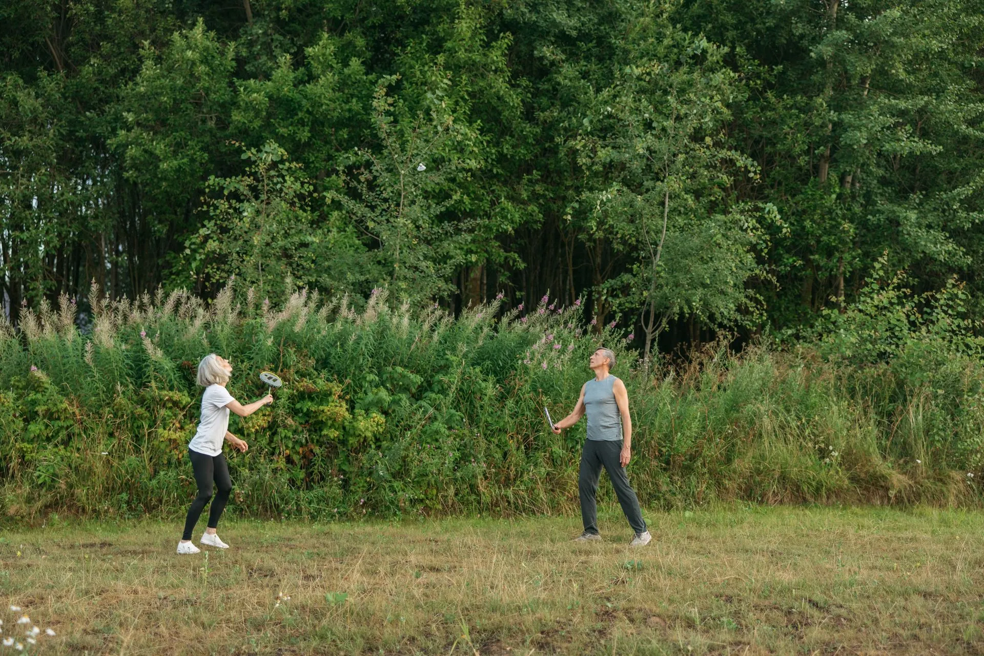 Een ouder stel speelt samen badminton in de buitenlucht.