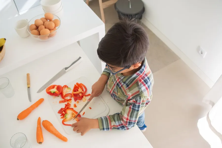 Kind snijdt paprika en groente in de keuken
