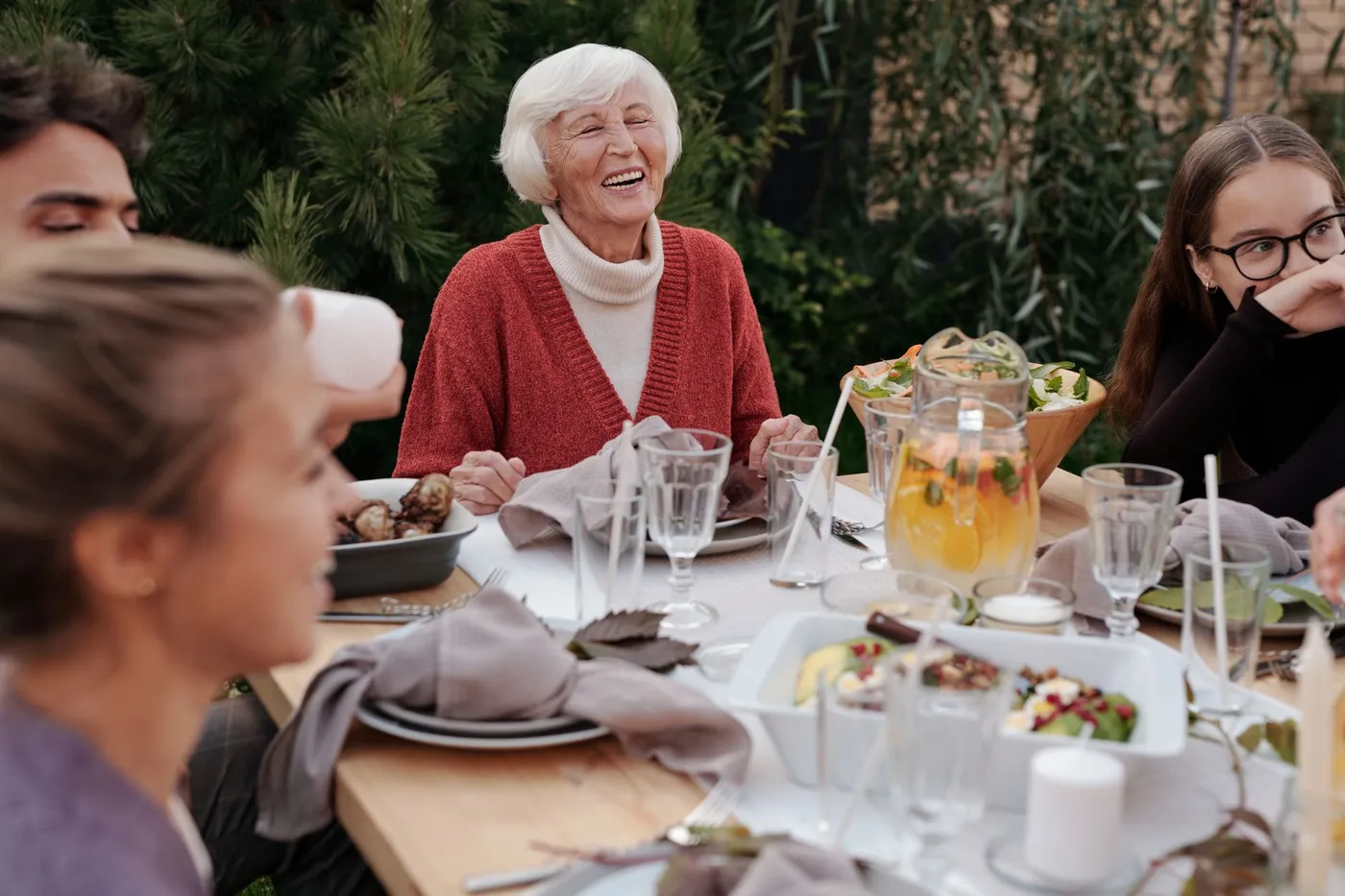 Lachende oudere vrouw aan tafel met familie en vrienden tijdens een maaltijd in de tuin