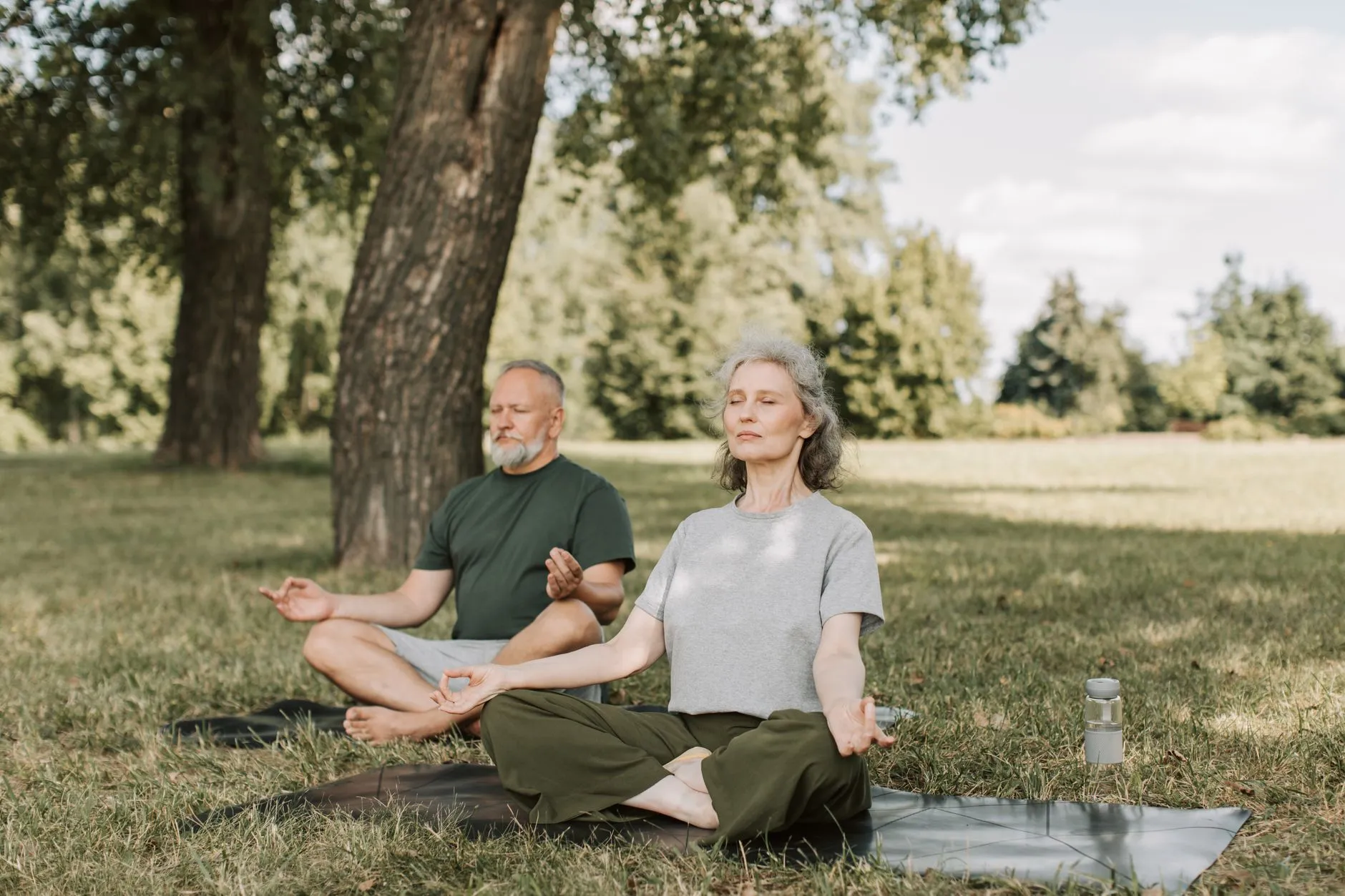 Een man en vrouw mediteren op matten in een park
