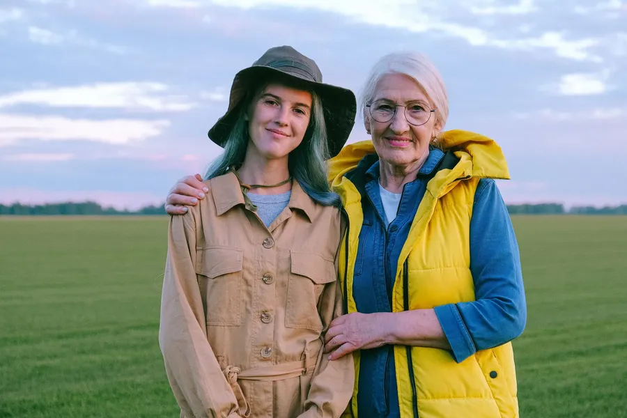een jonge vrouw en een oudere vrouw glimlachen samen in een open groen veld