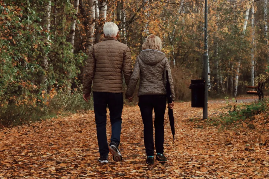 Ouder stel wandelt over een herfstpad, bewegen en mentale gezondheid