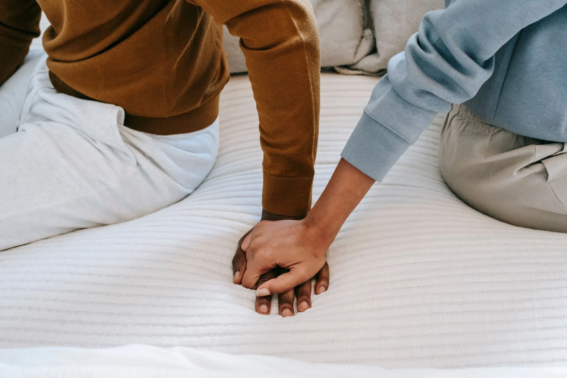 Twee mensen houden elkaars hand vast op bed