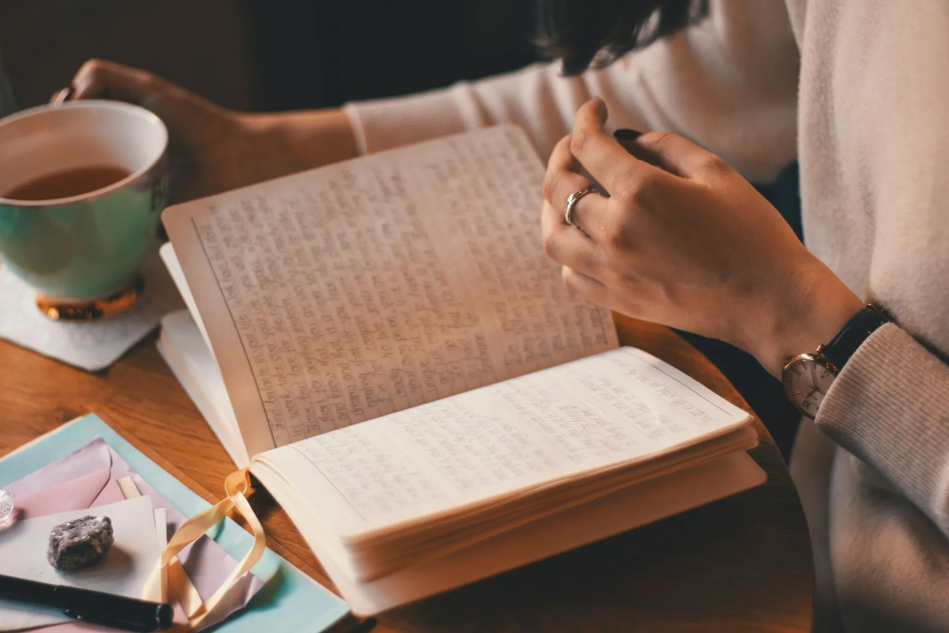 Vrouw schrijft in een dagboek met een kop koffie aan een houten tafel.