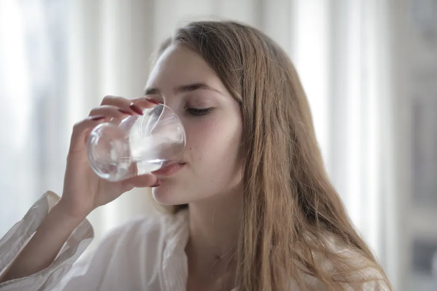 Vrouw drinkt een glas water bij het raam