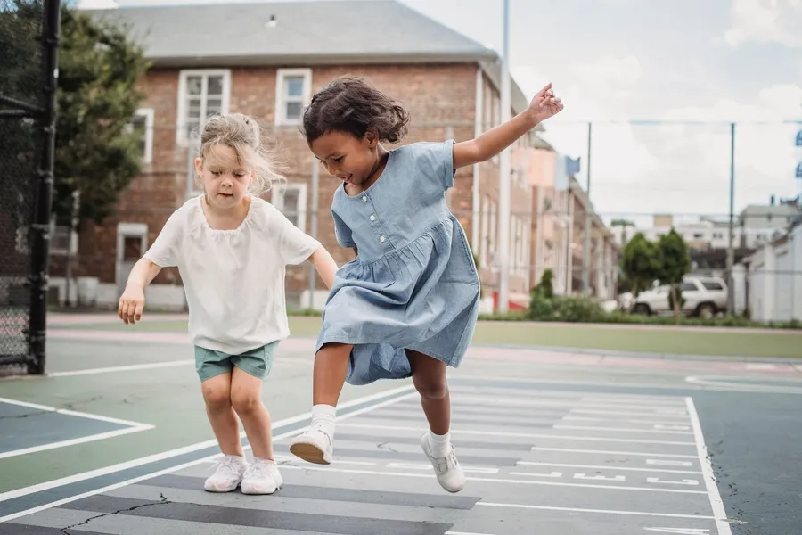 Twee kinderen hinkelen samen op een speelplein