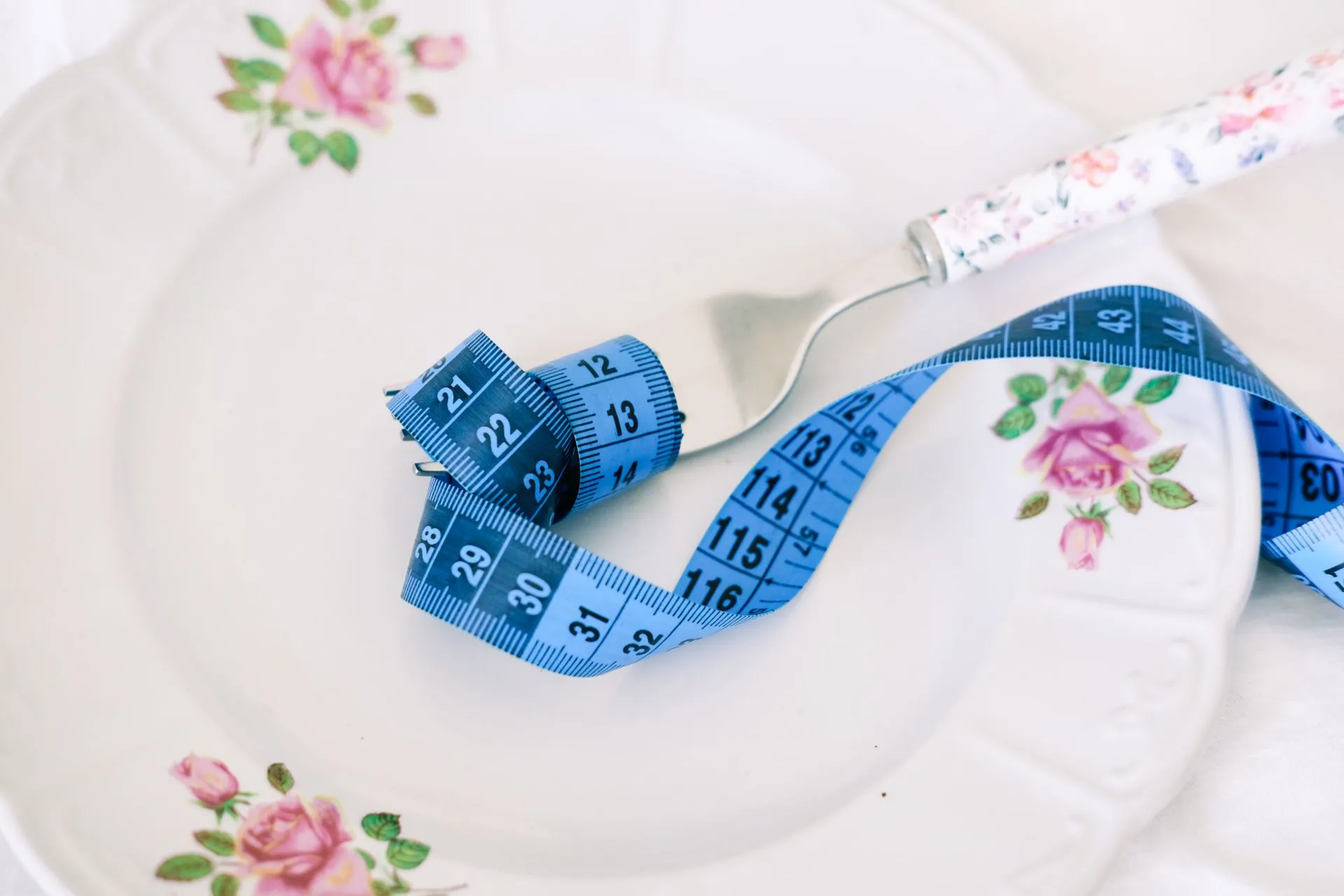 Bord met bloemmotief, vork en blauw meetlint als symbool voor gezond eten.