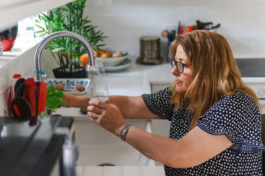 Vrouw van middelbare leeftijd vult een glas water in een moderne keuken.