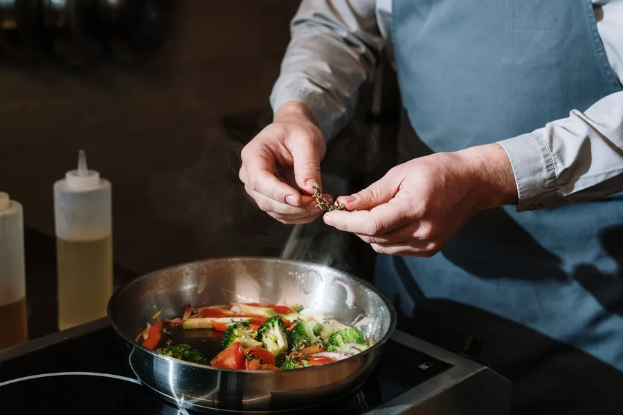 Iemand voegt kruiden toe aan groenten in een pan