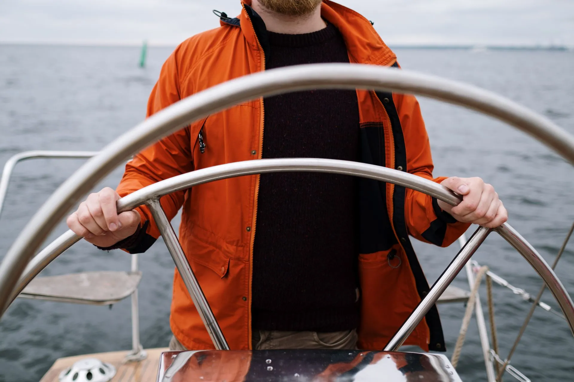 Close-up van een kapitein in oranje jas aan het stuurwiel van een boot op zee.