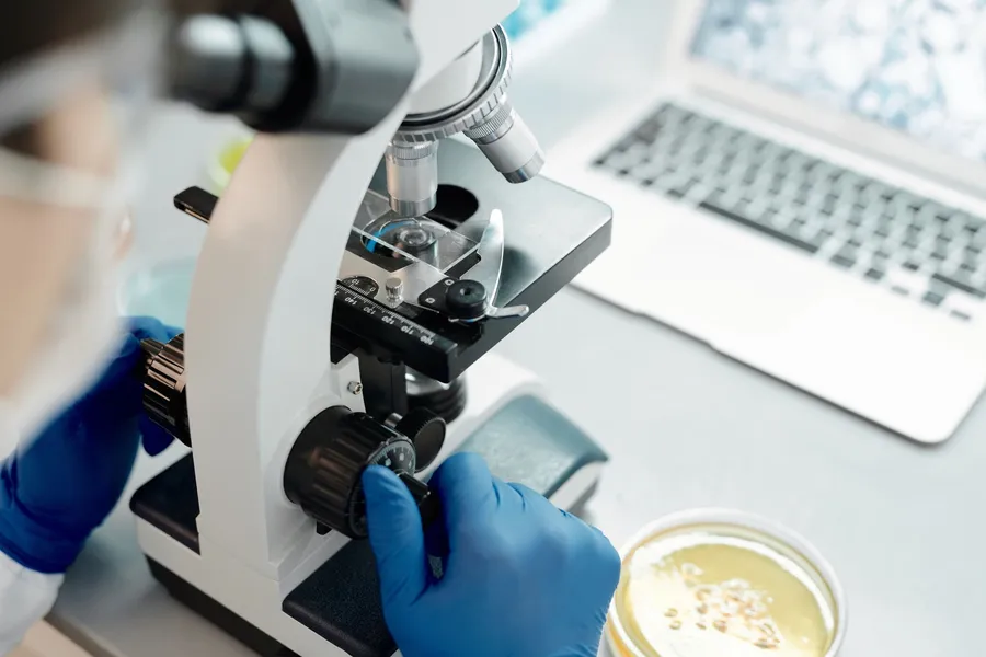 Onderzoeker bedient een microscoop met handschoenen aan