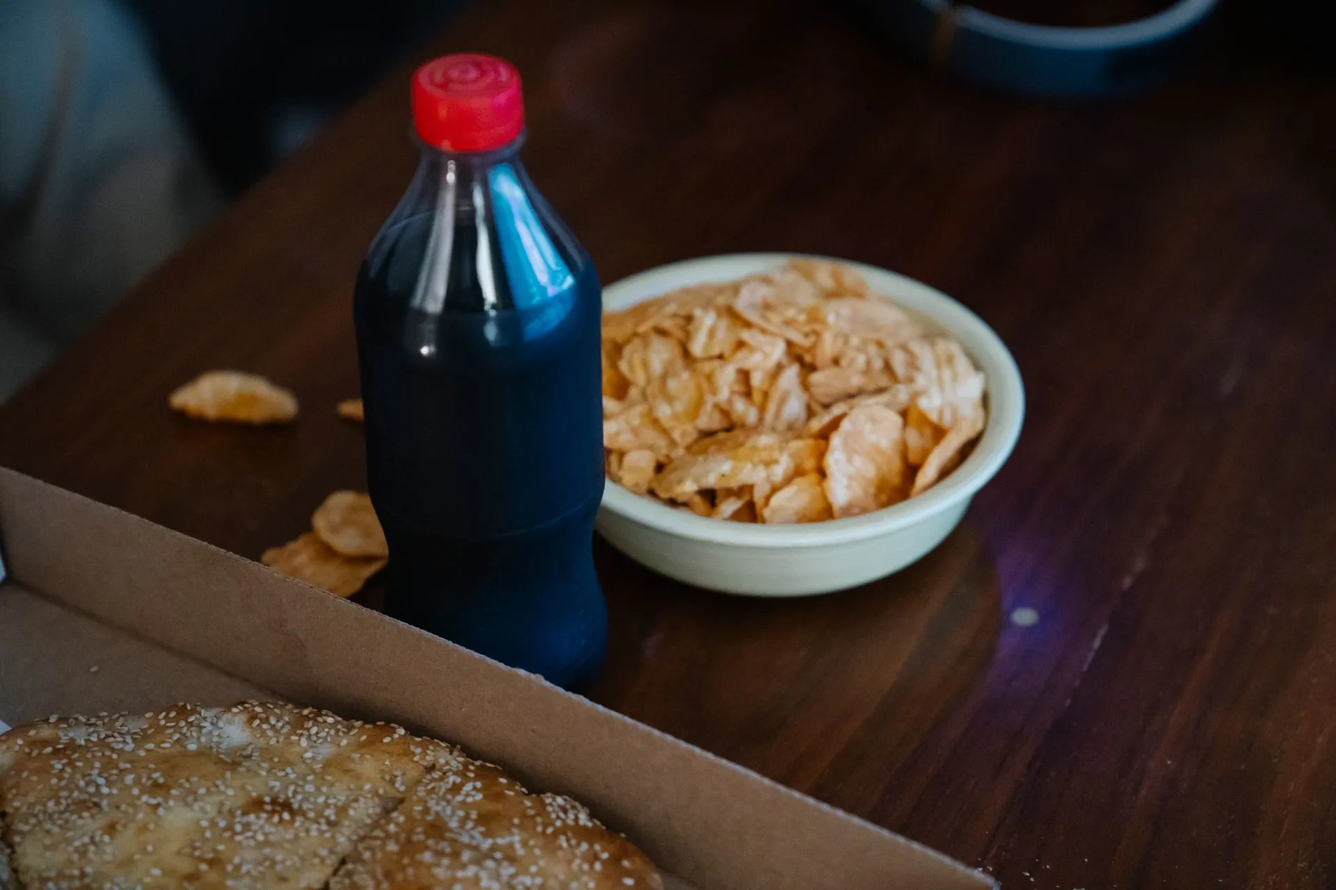 Frisdrankfles tussen afhaalpizza en chips, gezien van bovenaf.