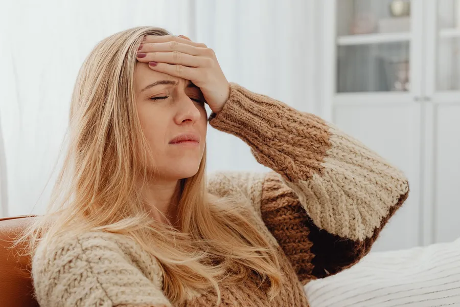 Vrouw zit met gesloten ogen en een hand op haar voorhoofd
