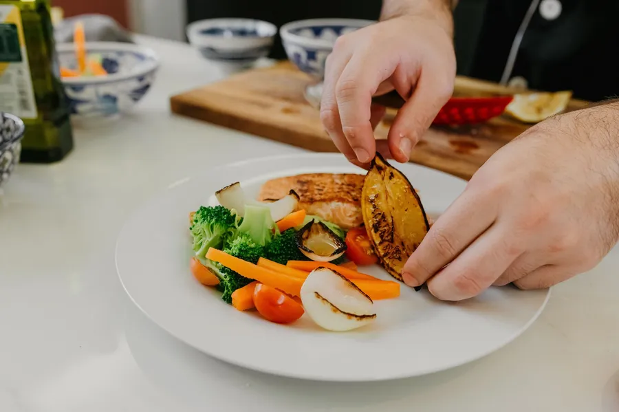 Handen snijden zalm bij een maaltijd met groente