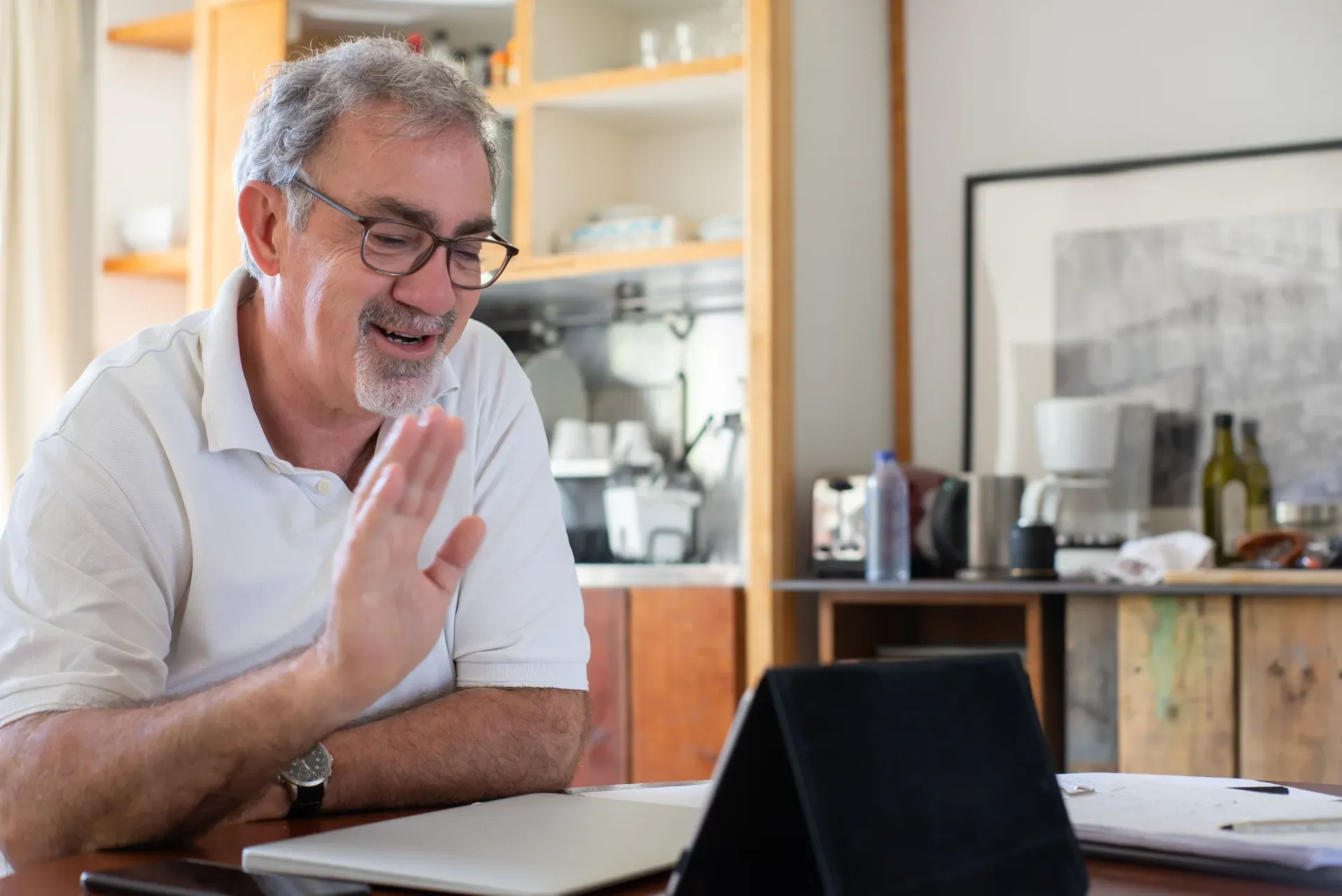 Man met grijs haar zit lachend aan de keukentafel achter een tablet