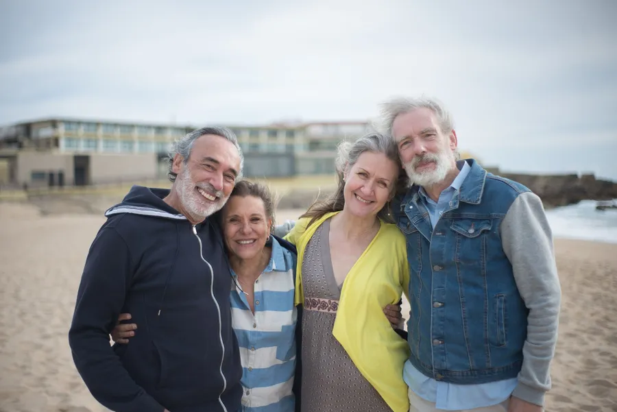 Vier volwassenen staan lachend naast elkaar op het strand