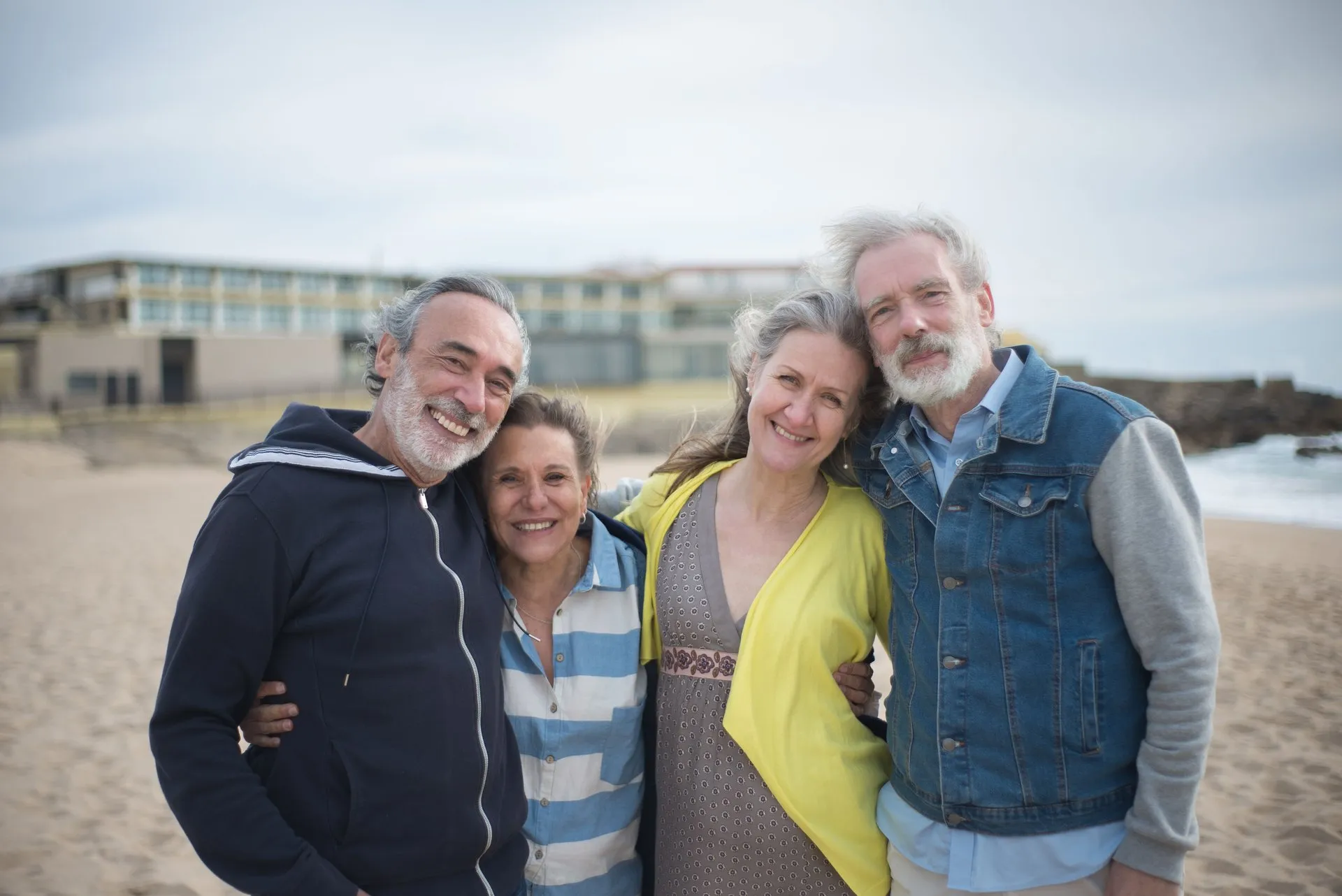 Vier volwassenen staan lachend naast elkaar op het strand