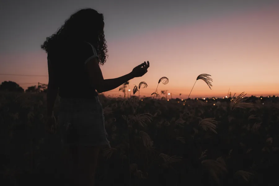 Vrouw kijkt vanuit hoog gras naar de ondergaande zon