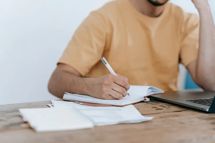 Man schrijft in een schrift naast een laptop
