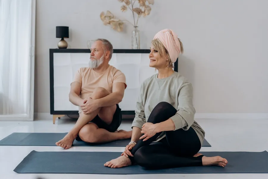 Oudere man en vrouw doen zittend yoga op matten