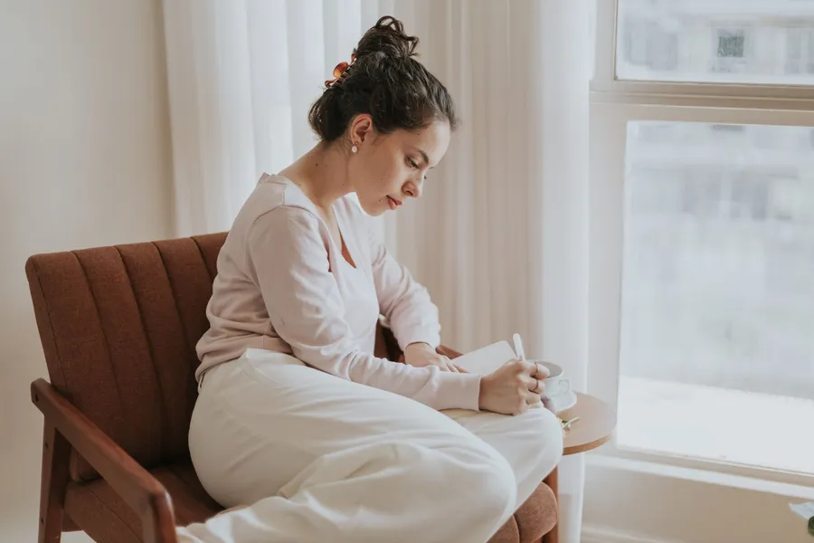 Vrouw schrijft in een notitieboek bij een raam