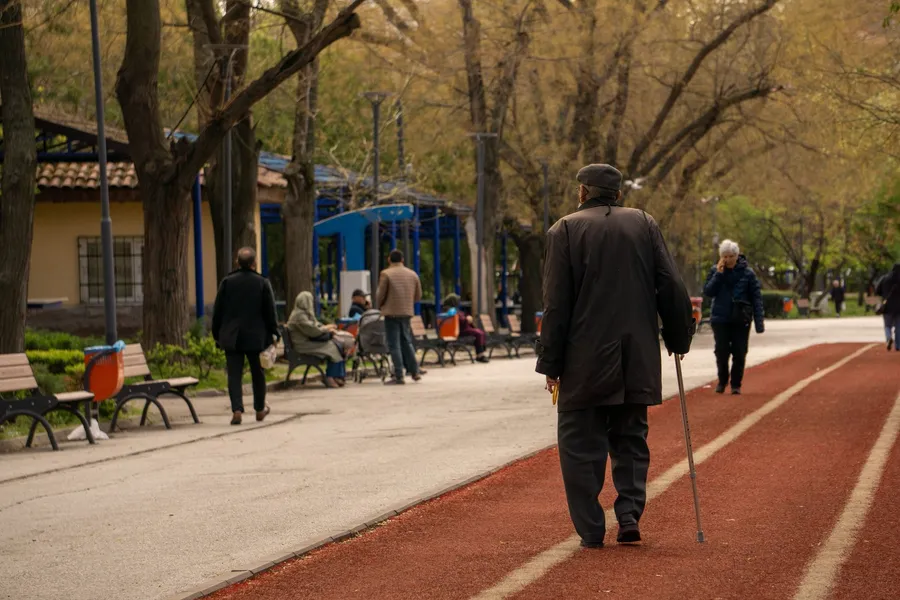 Oudere man wandelt met een stok over een parkpad