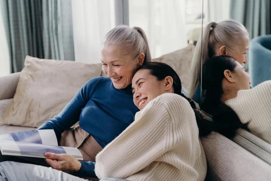 Oudere en jongere vrouw bekijken samen een fotoboek op de bank