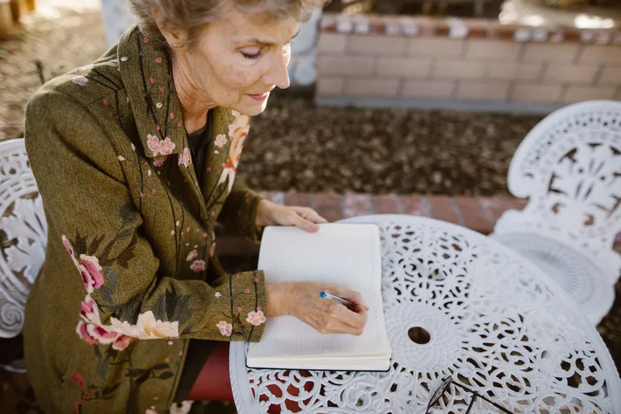 Oudere vrouw schrijft in een notitieboek aan een tuintafel