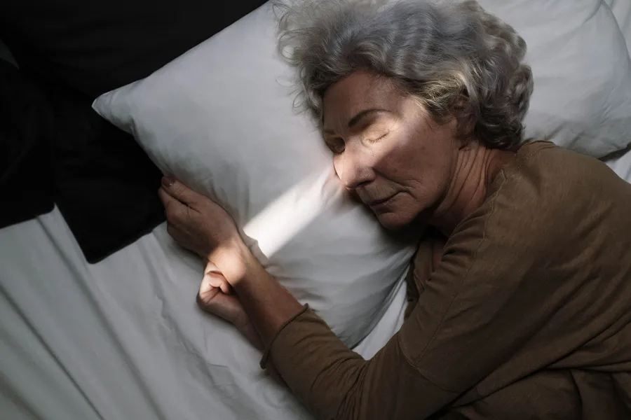 Oudere vrouw slaapt vredig in bed bij zacht licht.