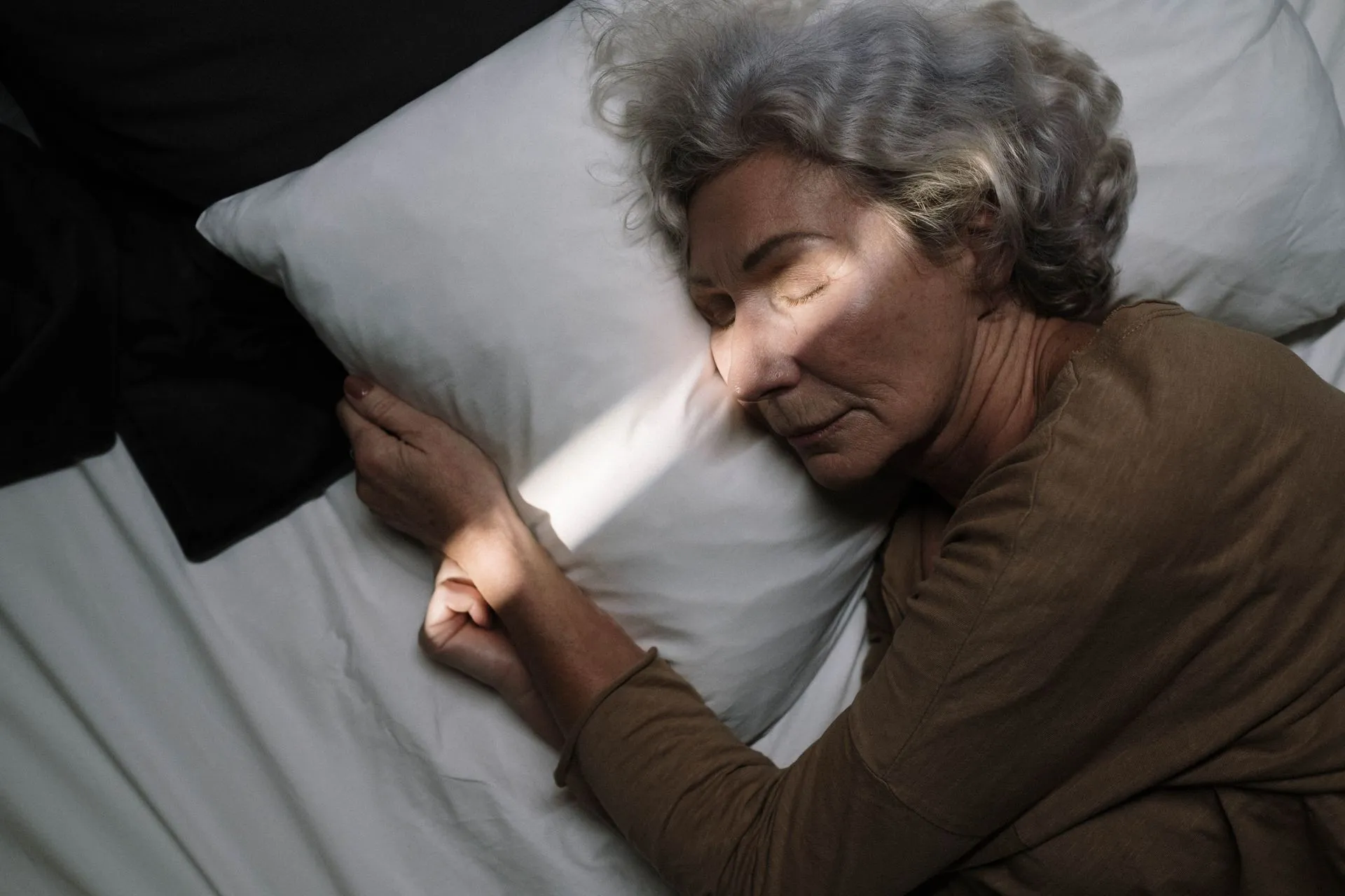 Oudere vrouw slaapt vredig in bed bij zacht licht.
