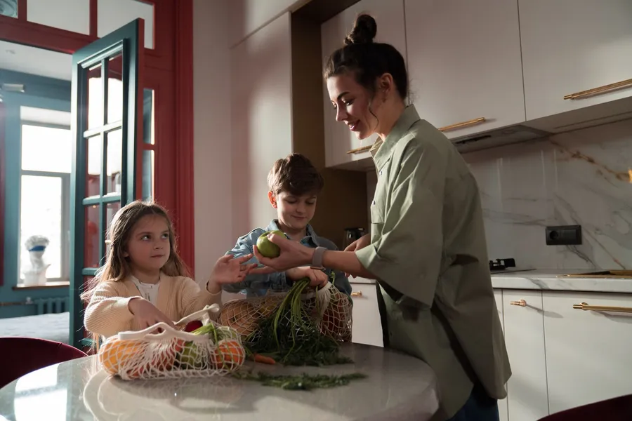 Vrouw en kinderen maken samen verse groenten klaar in een moderne keuken.