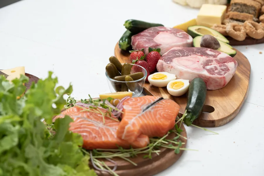 Verse keto-ingrediënten zoals zalm, rundvlees en groenten op houten planken.