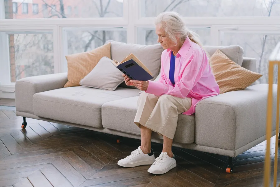 Oudere vrouw leest een boek op de bank