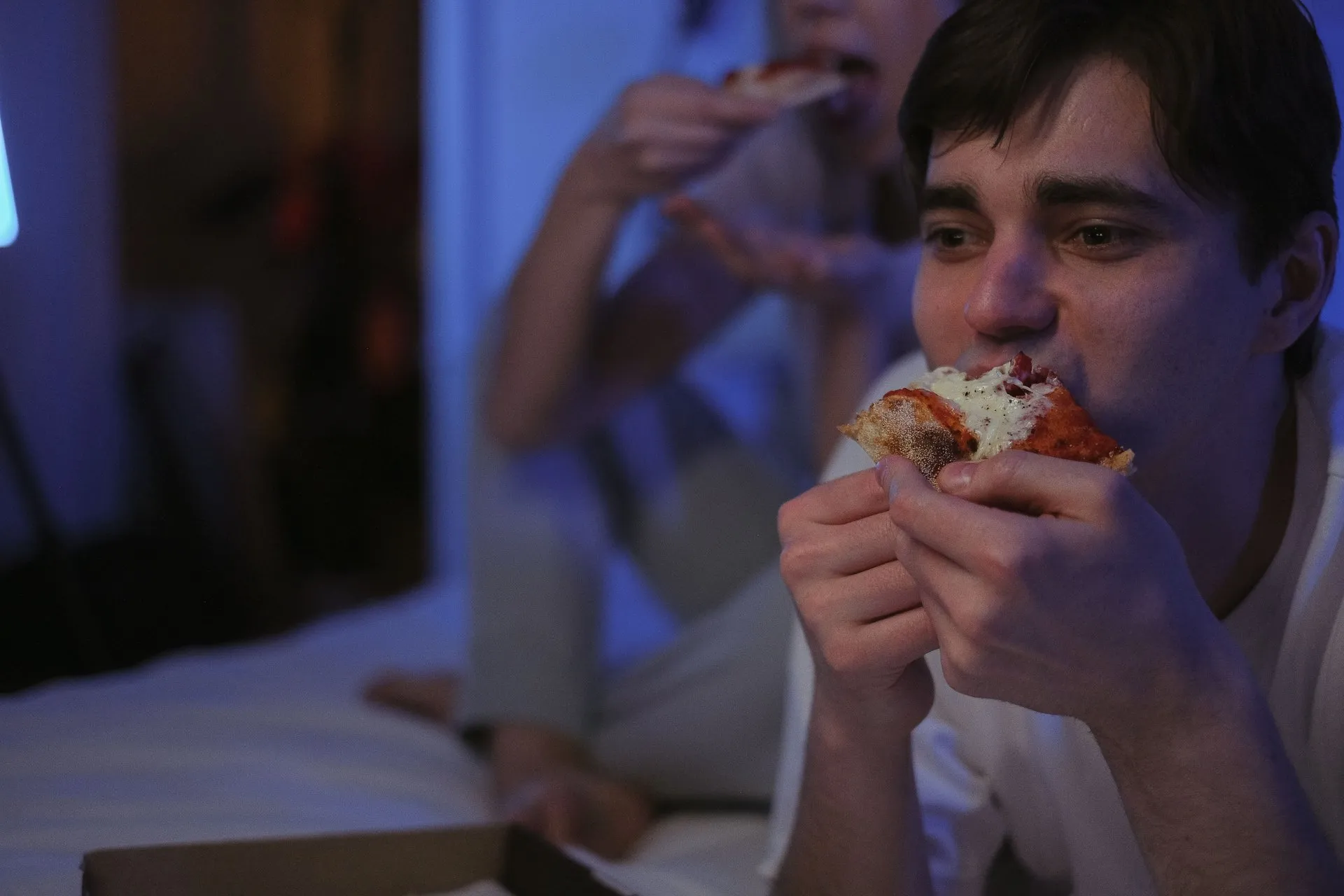 Man eet een stuk pizza bij gedimd licht