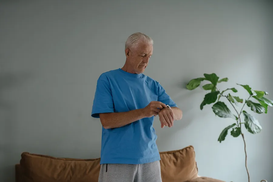 Oudere man bekijkt zijn sporthorloge in de woonkamer