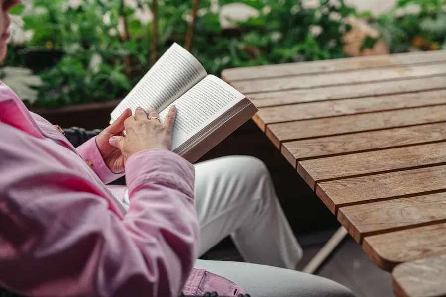 Vrouw leest buiten een boek aan een tafel