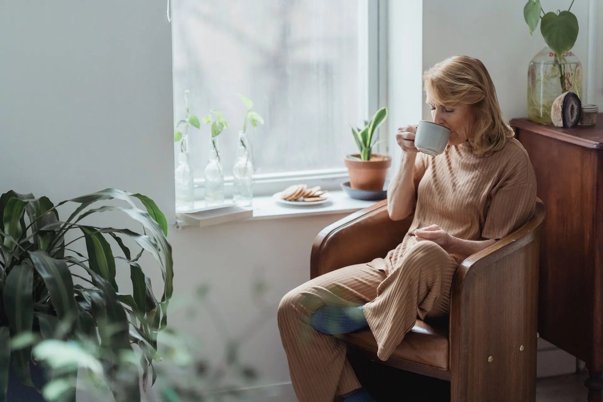 Vrouw drinkt uit een mok in een fauteuil bij het raam