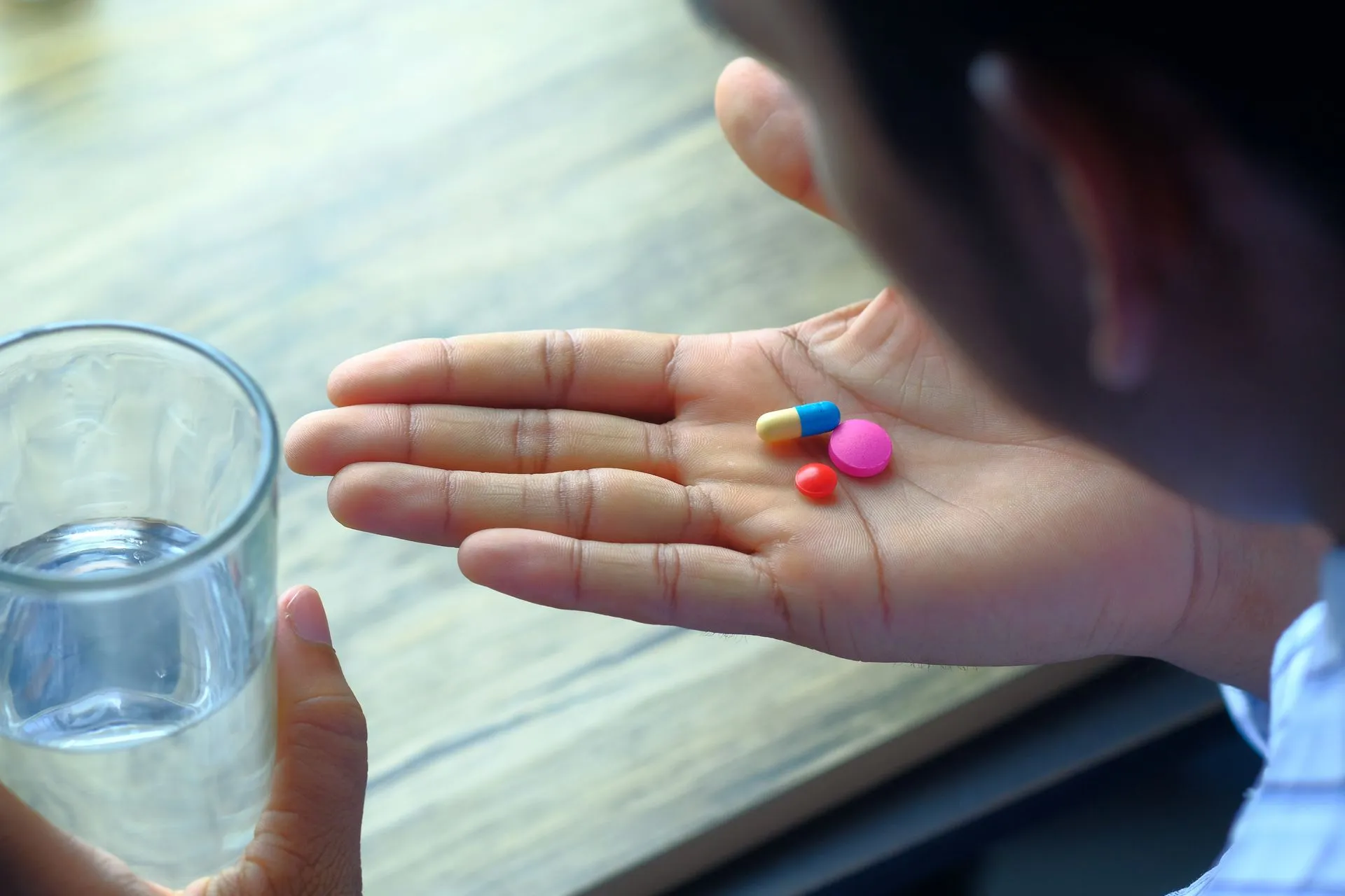 Hand met verschillende pillen naast een glas water.