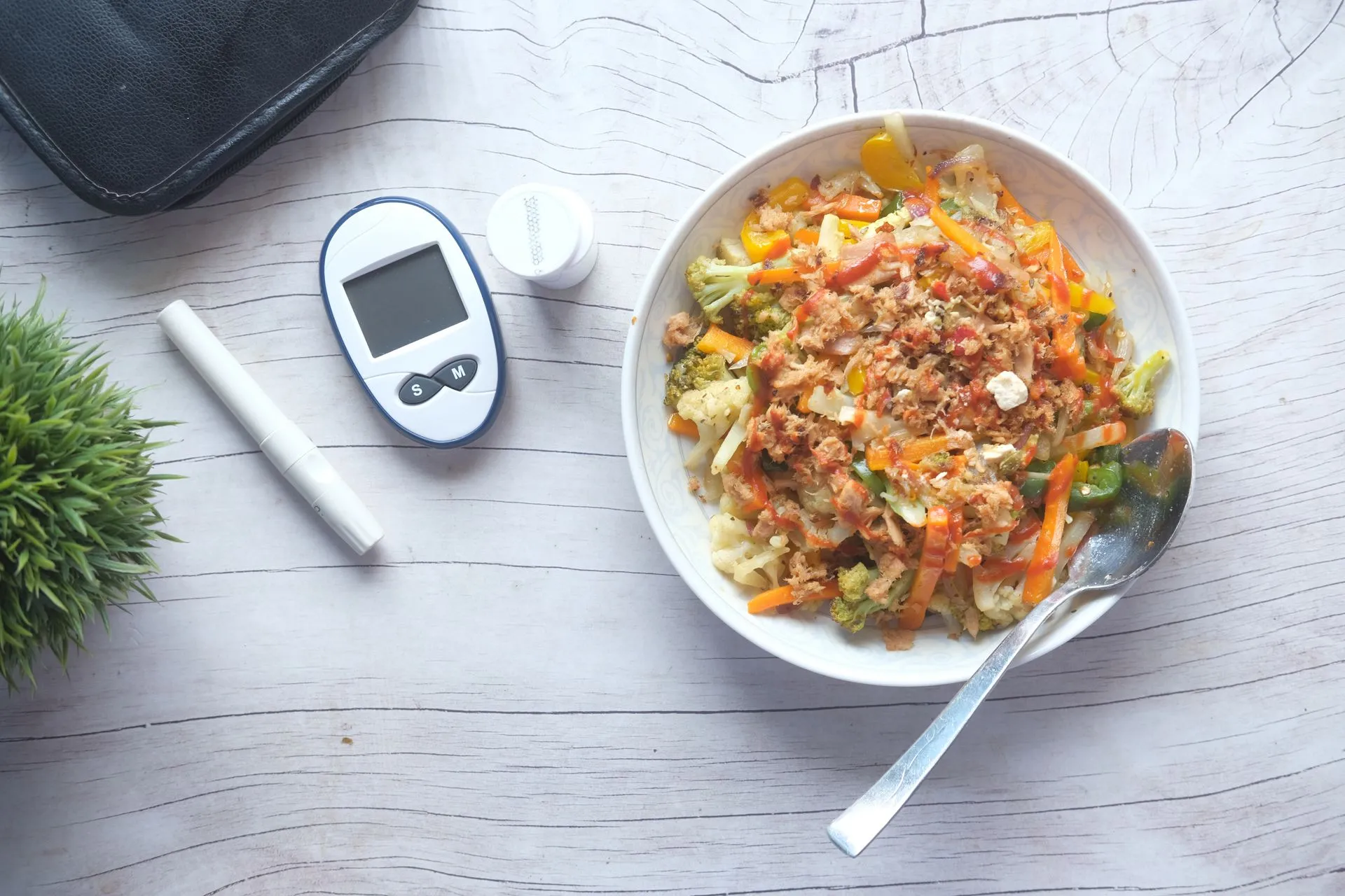 Groentesalade naast diabetesmeetapparatuur op een houten tafel, van bovenaf.