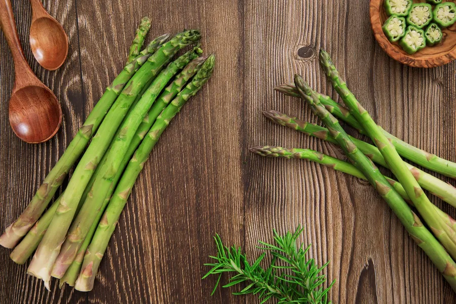 Verse asperges en kruiden op een rustieke houten tafel, van bovenaf.