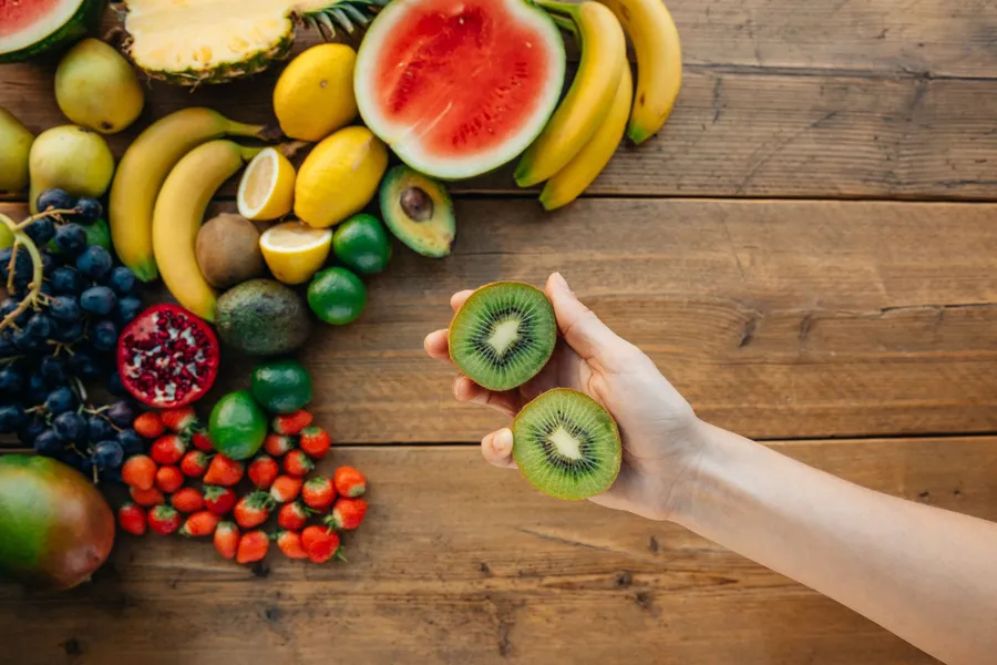 Handen houden een doorgesneden kiwi boven vers fruit