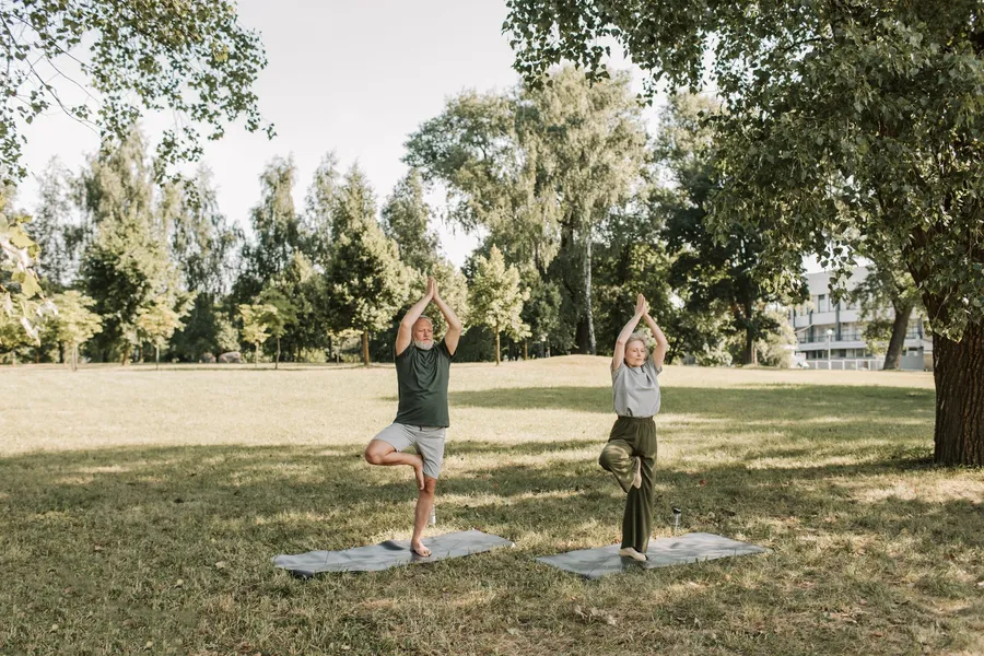 Ouder stel doet balansoefeningen op yogamatten in een park