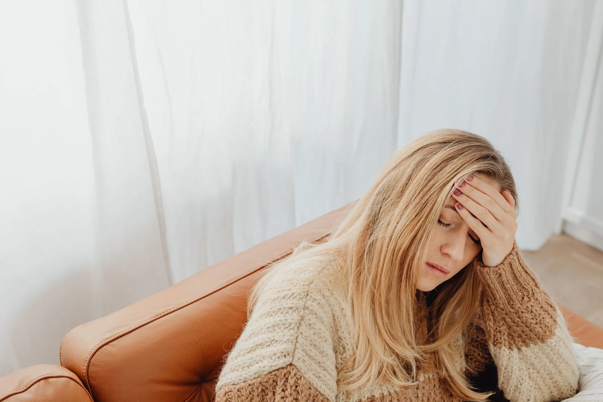 Vrouw in gebreide trui zit met hoofdpijn op de bank.