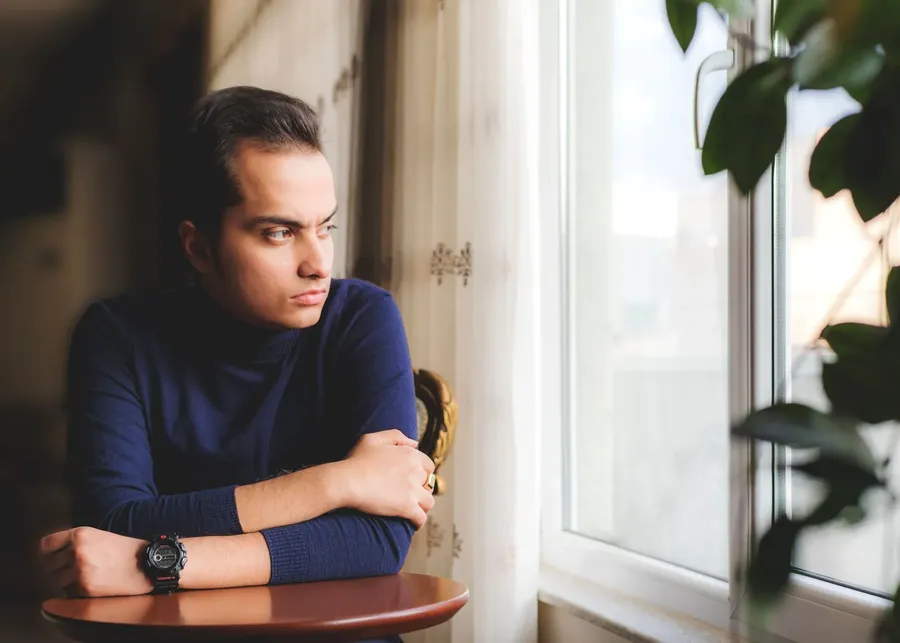 Jonge man leunt op een tafel en kijkt peinzend uit het raam
