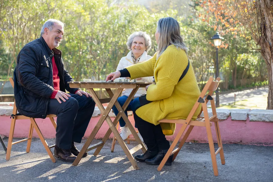 Oudere man en twee vrouwen praten en lachen samen aan een tafeltje buiten